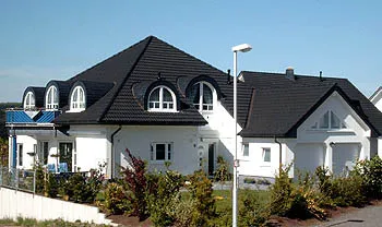 Weißes Einfamilienhaus mit dunklem Dach und Rundgauben